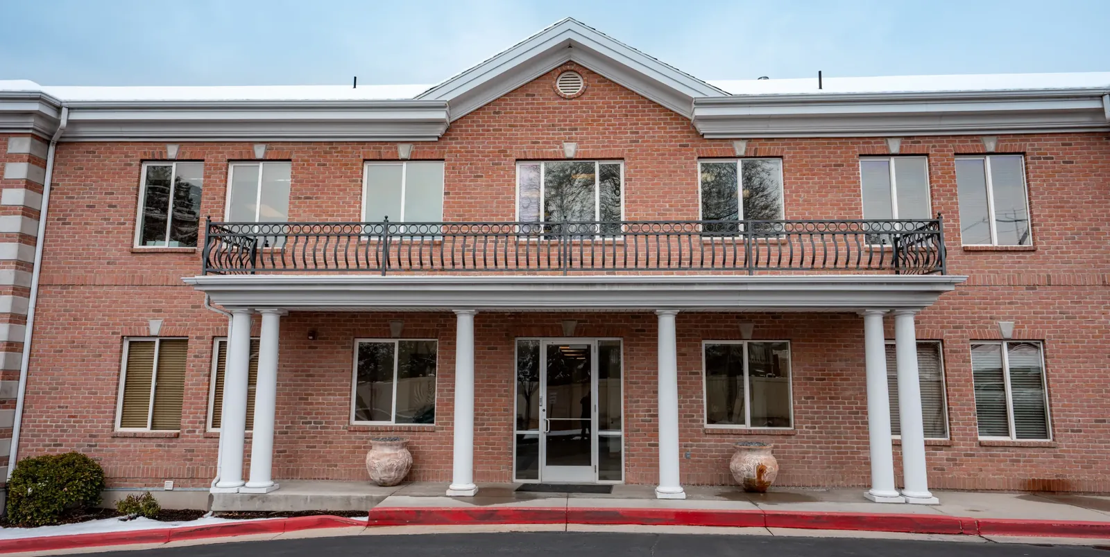 Red brick two-story building exterior with white columns supporting an upper balcony over the front entrance.