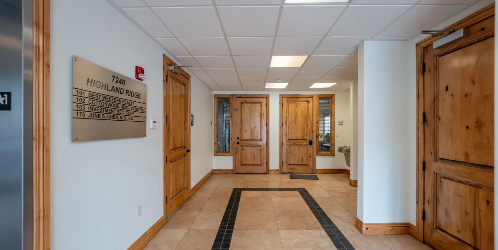 Office building hallway with wooden doors and a tenant directory sign.