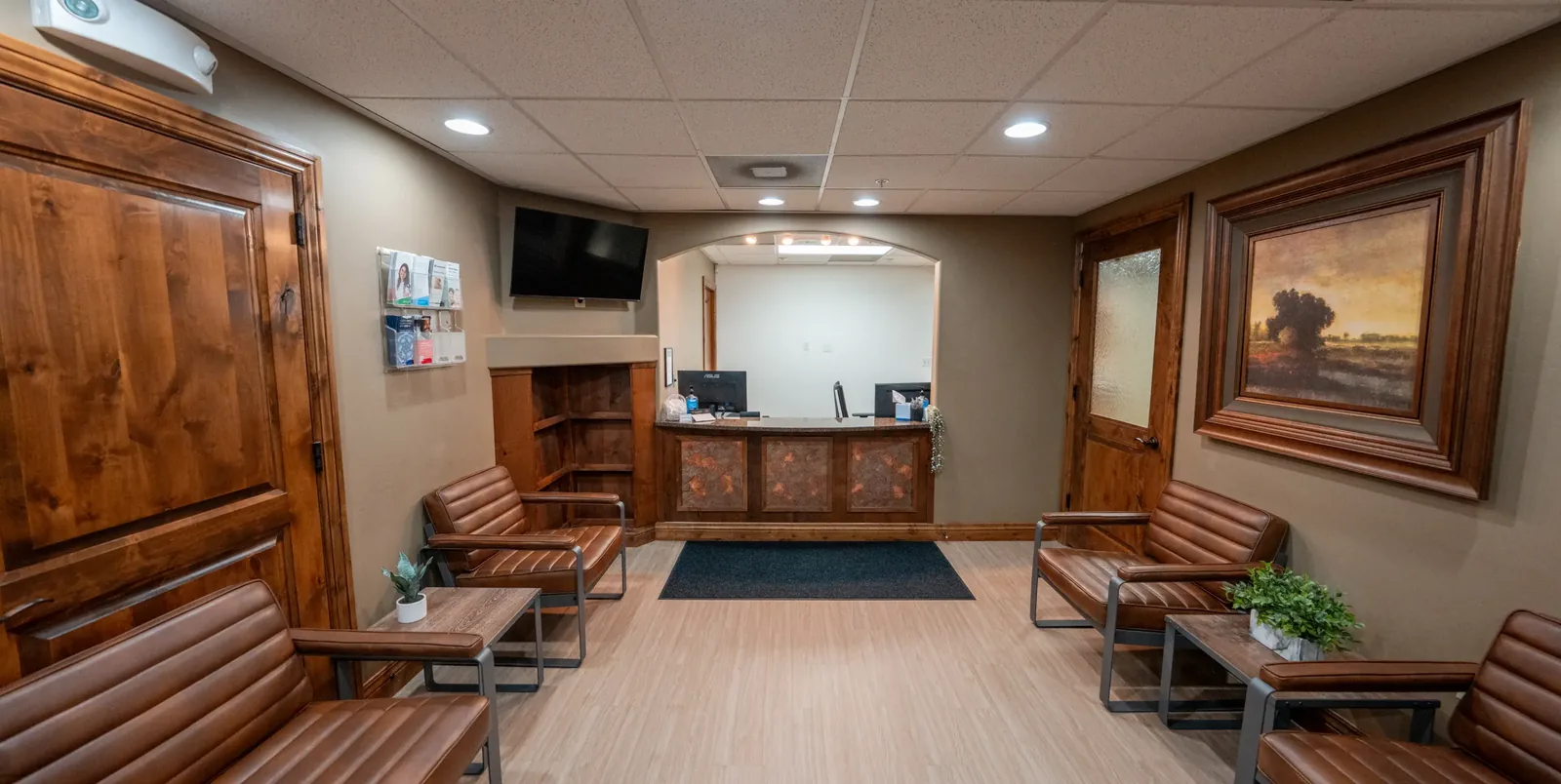 Dental office waiting area with leather armchairs, side tables, and a reception desk.